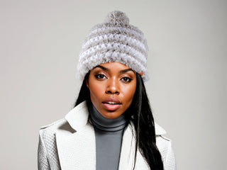 Woman wearing a white satin lined winter hat with a gray faux fur trim and pom.