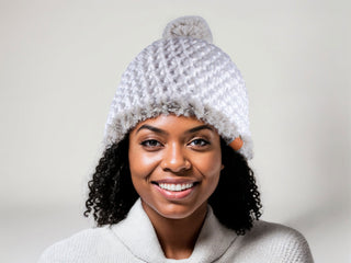 Woman with curly natural hair wearing a white satin lined winter hat with a gray faux fur trim and pom.