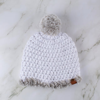 White satin lined winter hat with a gray faux fur trim and pom.